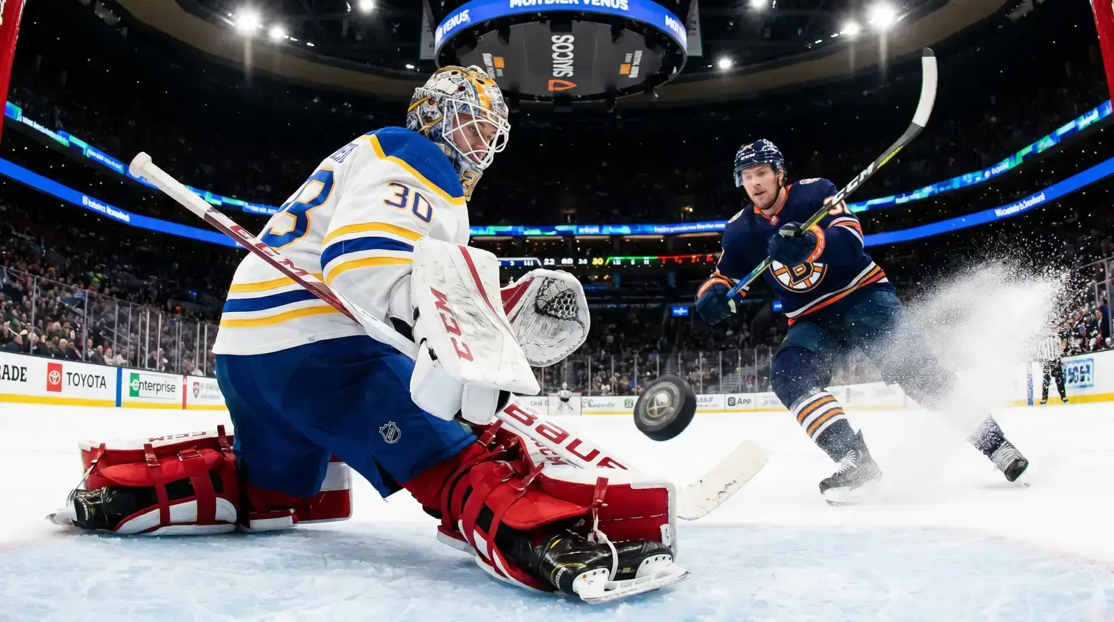 NHL players during live gameplay with a goaltender positioned deep in the crease tracking the puck